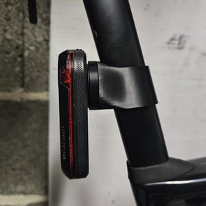 Könnte beinhalten: Ein schwarzes Fahrradrücklicht mit rotem Lichtstreifen ist an einer schwarzen Fahrradsattelstütze montiert. Das Rücklicht ist mit "OCARMIN" beschriftet. Das Licht wird mit einer schwarzen Halterung befestigt.