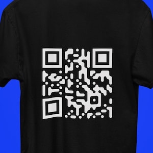 May include: Black t-shirt with a large white QR code printed on the back. The shirt is hanging on a wooden hanger against a blue background. The QR code is a complex pattern of black and white squares.