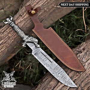 May include: A decorative dagger with a patterned blade and ornate silver handle featuring a dragon design. The dagger is paired with a brown leather sheath. The image includes the text "Legends of Vikings" and "Next Day Shipping".