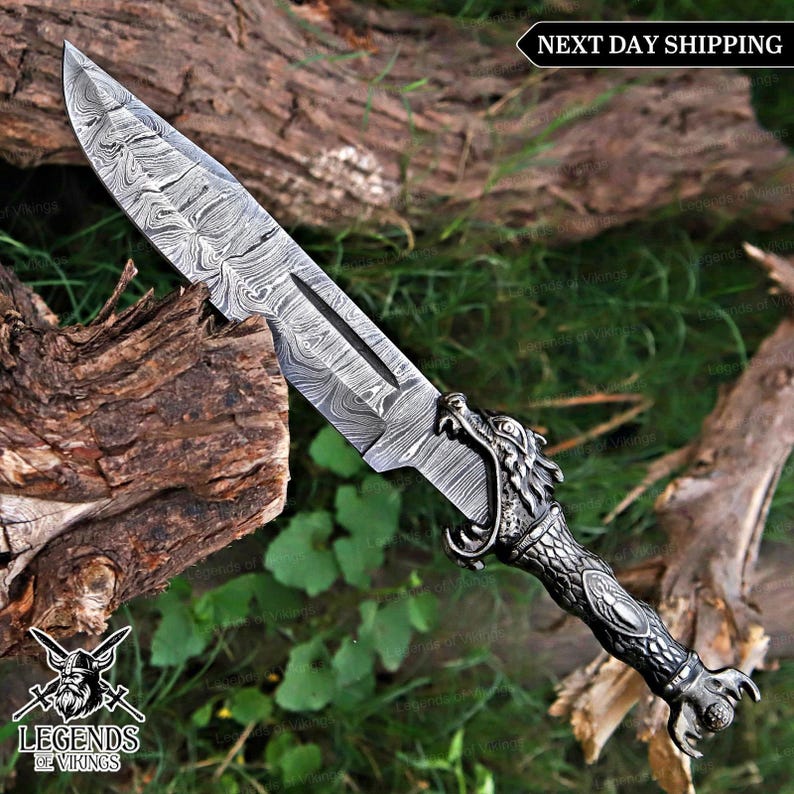 May include: A large, ornate knife with a patterned blade and a dragon-themed handle. The blade has a unique, swirling pattern. The handle features a dragon head and scales. The knife is set against a natural, outdoor background.