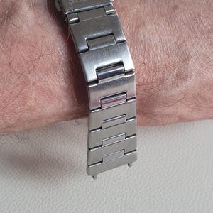 May include: A silver-toned stainless steel watch bracelet featuring a brushed finish and a folding clasp mechanism. The clasp is clearly engraved with the brand name SEIKO in capital letters. The bracelet consists of multiple rectangular links.