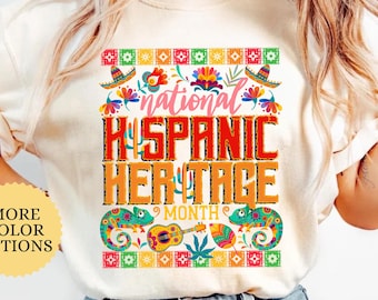 May include: Ivory-colored t-shirt with a colorful graphic celebrating National Hispanic Heritage Month. The design includes the text "National Hispanic Heritage Month" with decorative elements like sombreros, flowers, and chameleons. The shirt is a casual wear item.