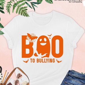 May include: White t-shirt with an orange graphic of a ghost with bats and the text "BOO TO BULLYING".