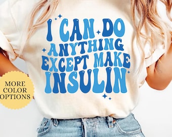 May include: Ivory-colored t-shirt with the text "I CAN DO ANYTHING EXCEPT MAKE INSULIN" in shades of blue. The shirt has a crew neck and short sleeves. The words "MORE COLOR OPTIONS" are also visible.