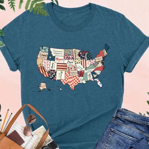 May include: A teal blue t-shirt with a patchwork design of the United States of America. The design includes words like "Loved", "Brave", and "Free".