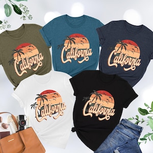 May include: Five t-shirts with a retro sunset graphic and the text "California" in a vintage font. The shirts are in various colors, including green, blue, navy, white, and black.