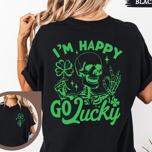 May include: Black t-shirt with a green graphic on the back that says "I'M HAPPY GO LUCKY" with a skeleton holding a four-leaf clover. The shirt also has a small graphic on the front.