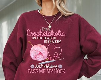 May include: A maroon sweatshirt with the text "I'm a Crochetaholic on the road to recovery. Just kidding. Pass me my hook."  The text is in white with a pink yarn ball and a crochet hook.