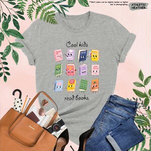 Puede incluir: Camiseta gris jaspeado con el texto "Cool kids read books". La camiseta presenta un gr&aacute;fico colorido de libros de dibujos animados. Se combina con vaqueros azules, un bolso tote marr&oacute;n y tacones negros.