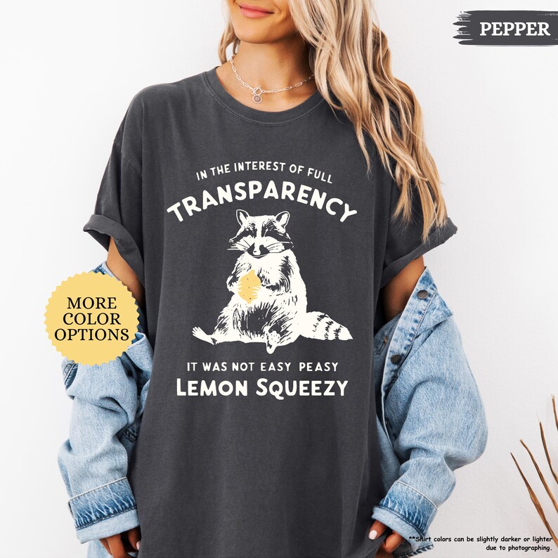 May include: A dark gray t-shirt with a raccoon graphic and the text "In the interest of full transparency it was not easy peasy lemon squeezy".