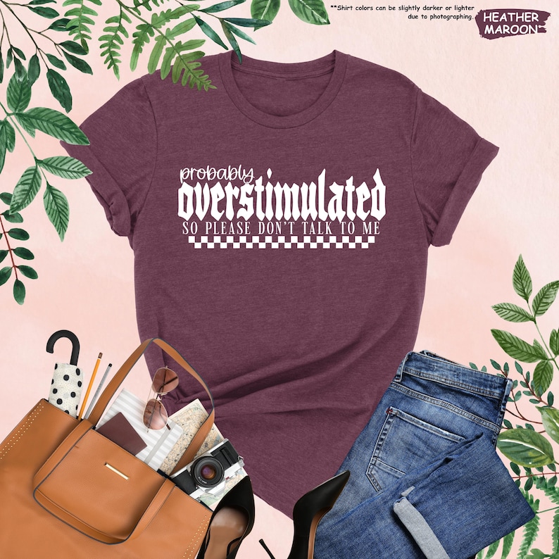 May include: Heather maroon t-shirt with white text that reads "probably overstimulated so please don't talk to me" with a checkered pattern underneath the text.