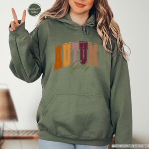 a woman in a green hoodie holding up a peace sign
