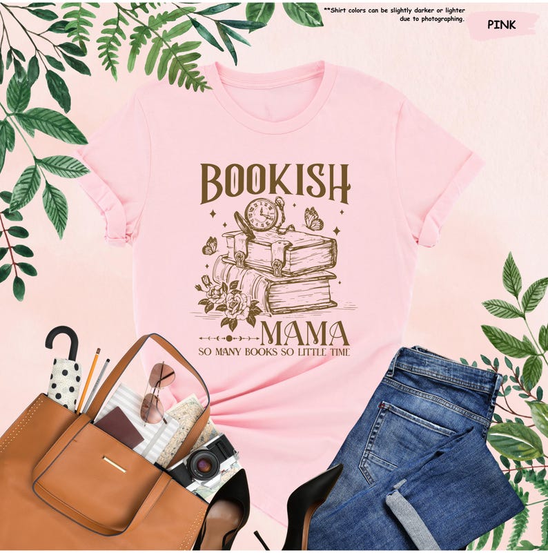 May include: Pink t-shirt with a graphic design featuring the words "BOOKISH MAMA" above a stack of books, a clock, and butterflies. The text "SO MANY BOOKS SO LITTLE TIME" is below the graphic. The shirt is displayed with a brown tote bag and blue jeans.