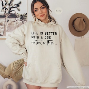 May include: A cream-colored hoodie with a black graphic that reads "Life is better with a dog - or two, or three..."