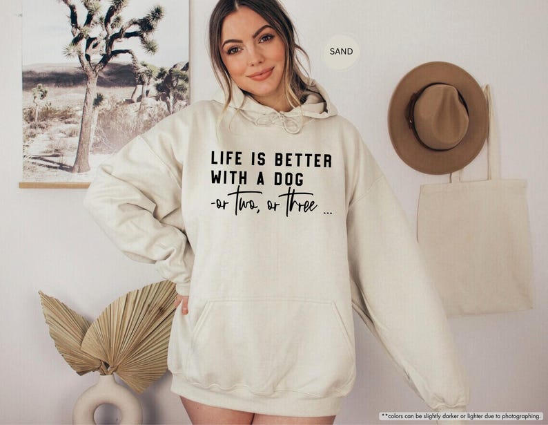 May include: A cream-colored hoodie with a black graphic that reads "Life is better with a dog - or two, or three..."