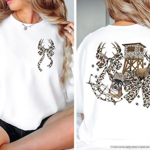 May include: White sweatshirt with a deer antler bow design on the front and back. The back features a deer, hunting blind, bow and arrow, and deer tracks, all in a camouflage pattern.