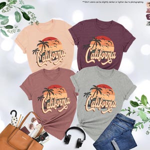 May include: Four t-shirts with a sunset and palm tree graphic and the text "California" in a retro font. The shirts are in heather peach, heather mauve, heather maroon, and athletic heather.