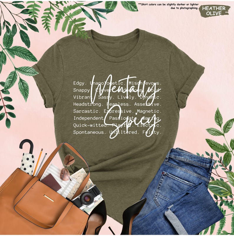K&ouml;nnte beinhalten: Olivgr&uuml;nes T-Shirt mit dem wei&szlig;en Schriftzug "Mentally Spicy". Das Shirt zeigt eine Liste von Adjektiven wie "Edgy", "Sassy" und "Fearless". Das Bild zeigt eine blaue Jeans und eine braune Tragetasche.