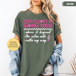 May include: Moss green t-shirt with the text "PLACES I WON'T BE GOING TODAY" in pink and white. The shirt also features the phrases "above & beyond", "the extra mile", and "outta my way". A button on the left says "MORE COLOR OPTIONS".