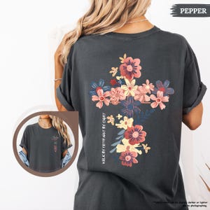 May include: A dark gray t-shirt with a floral cross design and the text "Walk by faith not by sight".
