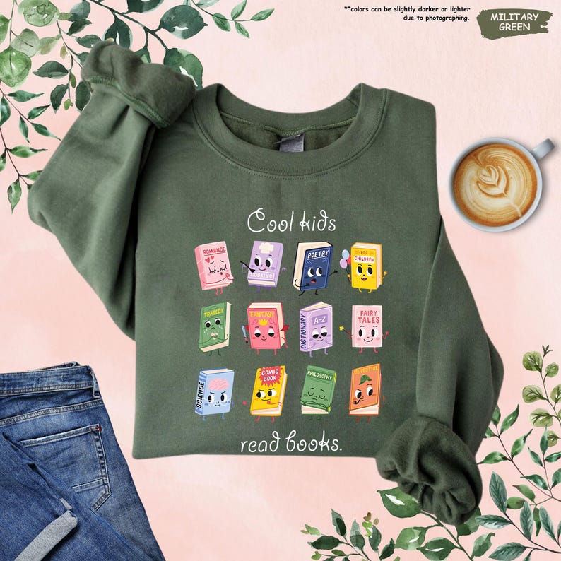 Puede incluir: Sudadera verde militar con el texto "Cool kids read books." El dise&ntilde;o presenta libros de dibujos animados con caras. La sudadera se combina con vaqueros azules y una taza de caf&eacute;. El color puede variar ligeramente.