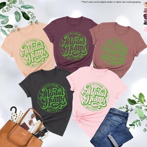 May include: Five different color t-shirts with a green graphic that says "All Day Every Day Mental Health Matters". The shirts are in the colors peach, heather mauve, maroon, dark grey heather, and pink.