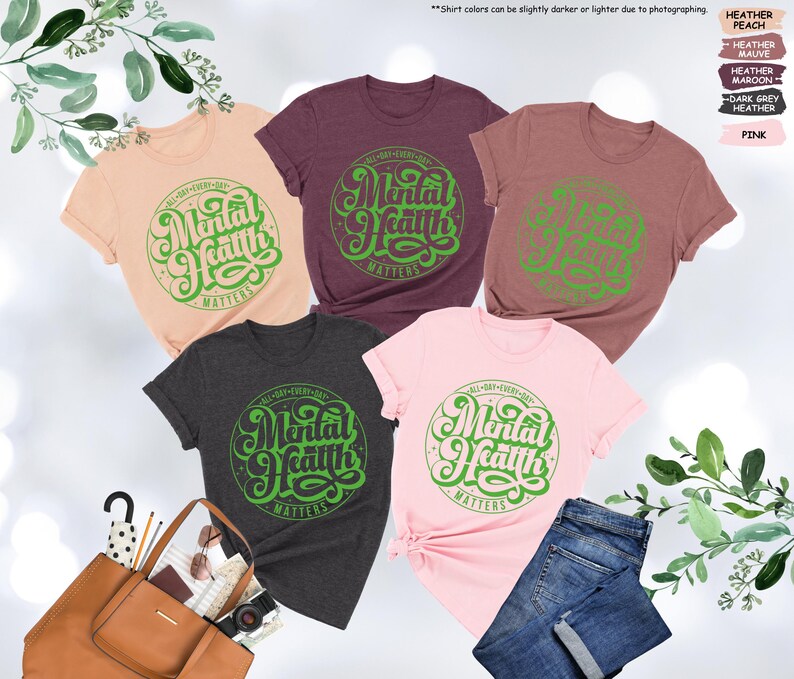 May include: Five different color t-shirts with a green graphic that says "All Day Every Day Mental Health Matters". The shirts are in the colors peach, heather mauve, maroon, dark grey heather, and pink.