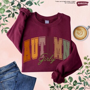 a maroon shirt with the word autumn on it next to a pair of jeans and