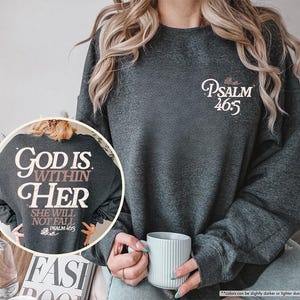 Puede incluir: Sudadera gris oscuro con el texto "Psalm 46:5" en escritura blanca en la parte delantera. La parte trasera de la sudadera presenta el texto "God is within her, she will not fall, Psalm 46:5" en una fuente estilizada.