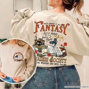 May include: A beige sweatshirt with a graphic print of a stack of books, a skull, and the text "Proud Member of the Fantasy Readers Society. Lost in fantasy found in books. Dragons, Wizards and Epic Tales".