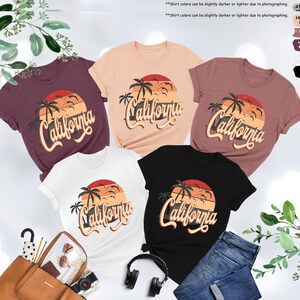 May include: Five t-shirts with a sunset and palm tree graphic and the text "California" in a retro font. The shirts are in various colors including white, black, pink, maroon, and light brown.