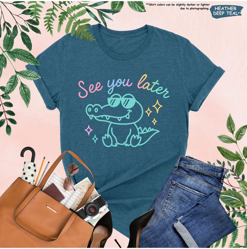 May include: A teal t-shirt with the phrase "See you later" and a cartoon alligator wearing sunglasses. The graphic is in pastel colors. The shirt is paired with blue jeans, a brown tote bag, and black heels.