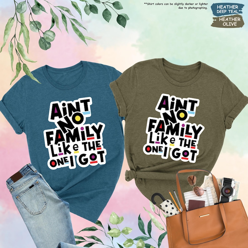 May include: Two t-shirts, one deep teal and one heather olive, each with the text "Ain't No Family Like The One I Got" in a colorful, bold font. The teal shirt is paired with jeans, while the olive shirt is next to a brown tote bag.