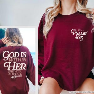 Puede incluir: Sudadera granate con texto blanco. La parte delantera muestra "Psalm 46:5" en escritura cursiva. La parte trasera presenta "God is Within Her, She Will Not Fall, Psalm 46:5". Una prenda casual de manga larga.