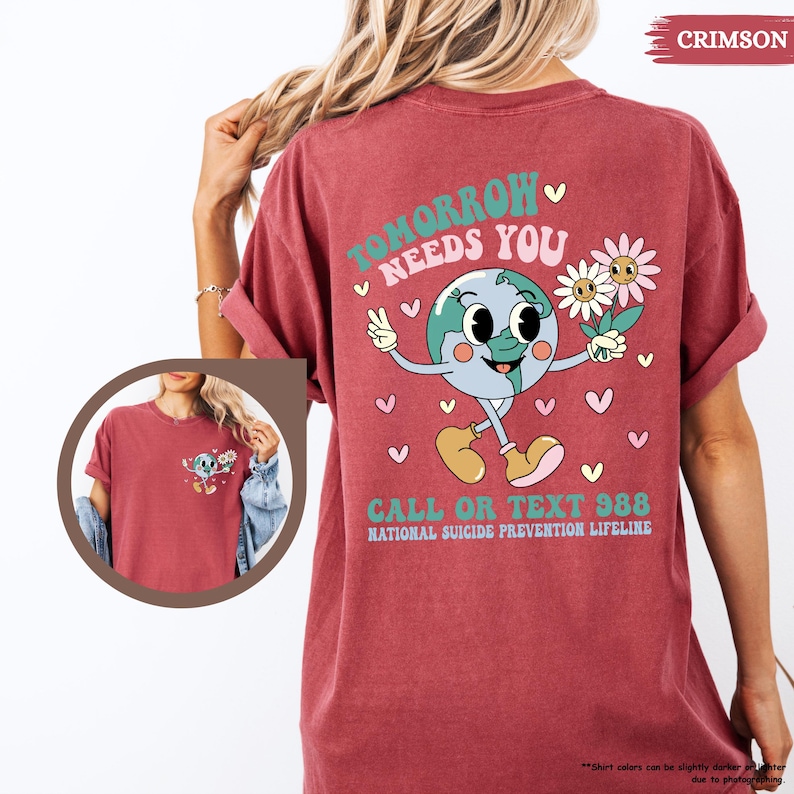 May include: Crimson t-shirt featuring the text "Tomorrow Needs You" and a cartoon earth character holding flowers. The shirt also includes the text "Call or Text 988, National Suicide Prevention Lifeline."