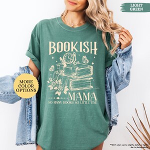 May include: Light green t-shirt featuring the words "BOOKISH MAMA" and a graphic of books, a clock, butterflies, and flowers. The phrase "SO MANY BOOKS SO LITTLE TIME" is below the graphic. A button on the left says "MORE COLOUR OPTIONS".
