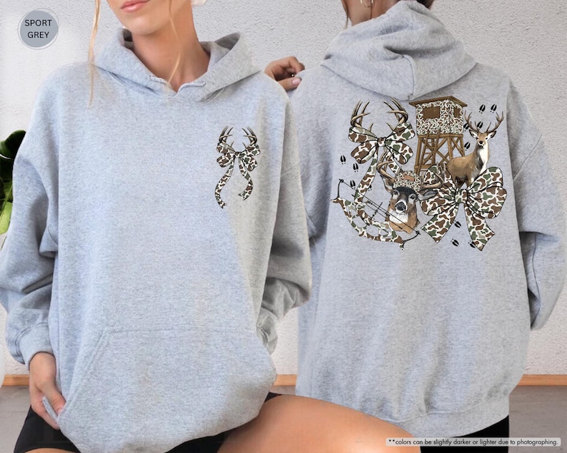 May include: Sport grey hoodie with a front pocket and a hood. The front features a bow with deer antlers in a camouflage pattern. The back displays a hunting scene with deer, a bow, and a deer stand, all in a camouflage bow design.