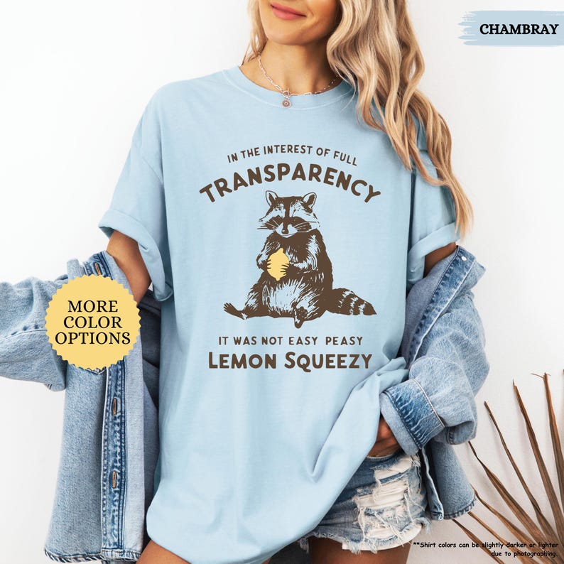 May include: A light blue t-shirt with a raccoon graphic holding a lemon. The text on the shirt reads "In the interest of full transparency, it was not easy peasy lemon squeezy."