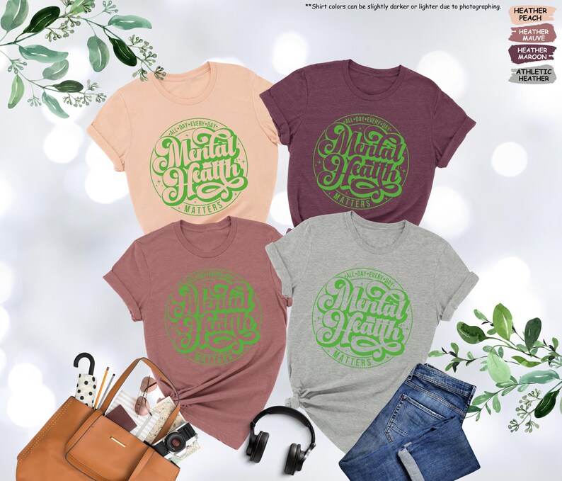 May include: Four t-shirts in different colors with the text "All Day Every Day Mental Health Matters" in a green circle on the front.