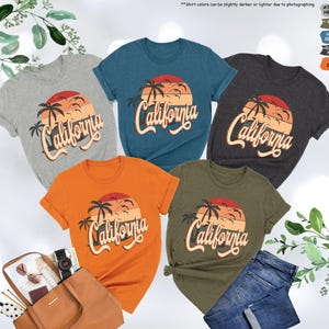 May include: Five t-shirts in different colors featuring a sunset graphic with palm trees and the text "California". The colors are grey, teal, dark grey, orange, and olive.
