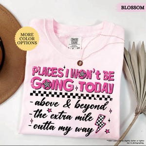 May include: A light pink t-shirt with the text "PLACES I WON'T BE GOING TODAY" in a distressed pink font. The shirt also features the phrases "above & beyond", "the extra mile", and "outta my way". A gold necklace is draped over the shirt.