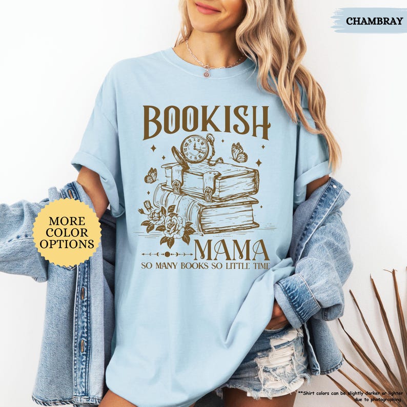 May include: Pale blue t-shirt featuring the text "BOOKISH MAMA" above a graphic of books, a clock, butterflies, and flowers. The phrase "SO MANY BOOKS SO LITTLE TIME" is below the graphic. The shirt is part of the "Chambray" colour options.