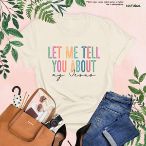 May include: A beige t-shirt with the text "LET ME TELL YOU ABOUT my Jesus" in rainbow colors. The text is in a retro font style.