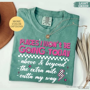 May include: A light green t-shirt with the text "PLACES I WON'T BE GOING TODAY" in pink. The shirt has a crew neck and short sleeves. A silver necklace with a pendant is on the shirt.