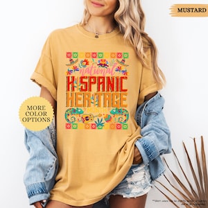 Peut inclure: T-shirt moutarde avec l'inscription "National Hispanic Heritage Month" dans un design color&eacute;. Le t-shirt pr&eacute;sente une bordure d&eacute;corative avec des sombreros, des fleurs et des instruments de musique. Les mots "More Color Options" sont &eacute;galement visibles.
