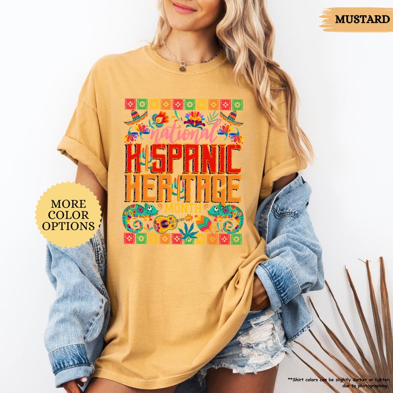 Peut inclure: T-shirt moutarde avec l'inscription "National Hispanic Heritage Month" dans un design color&eacute;. Le t-shirt pr&eacute;sente une bordure d&eacute;corative avec des sombreros, des fleurs et des instruments de musique. Les mots "More Color Options" sont &eacute;galement visibles.
