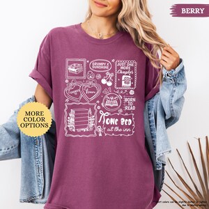 Puede incluir: Camiseta de color bayas con dise&ntilde;os gr&aacute;ficos blancos que incluyen libros, corazones y el texto "Grumpy x Sunshine", "Just One More Chapter" y "One Bed at the Inn". Incluye un bot&oacute;n "More Color Options".