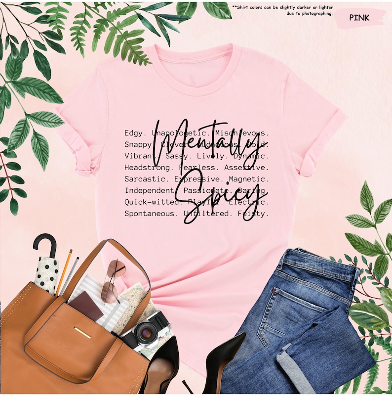 K&ouml;nnte beinhalten: Ein rosa T-Shirt mit den Worten "Mentally Spicy" in einer stilvollen Schriftart. Das Shirt listet auch mehrere Adjektive wie "Edgy", "Sassy" und "Fearless" auf. Das Shirt wird mit einer blauen Jeans, einer braunen Handtasche und schwarzen Abs&auml;tzen kombiniert.