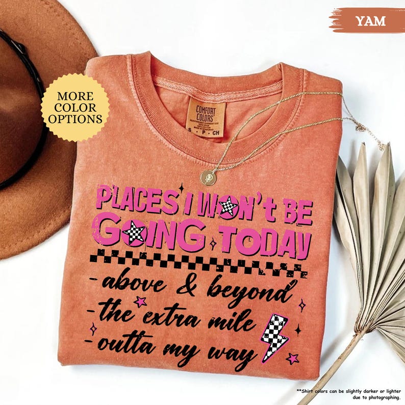 May include: A yam-colored t-shirt with the text "PLACES I WON'T BE GOING TODAY" in pink and black. The shirt has a crew neck and a gold necklace. The shirt also has the phrases "above & beyond", "the extra mile", and "outta my way".