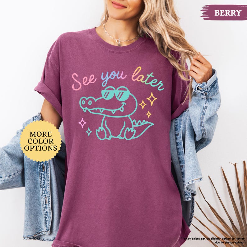 Puede incluir: Camiseta de color baya con la frase "See you later" y un cocodrilo de dibujos animados con gafas de sol. El cocodrilo est&aacute; delineado en turquesa, con texto rosa y amarillo. La camiseta tambi&eacute;n tiene un bot&oacute;n "More Color Options".